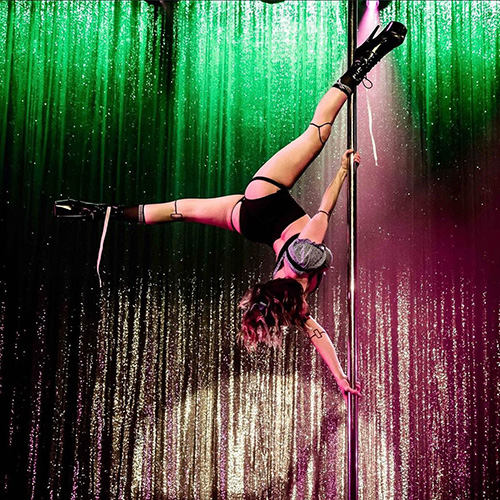Pole dancer performing an extended butterfly trick on a competition stage with dynamic lighting
