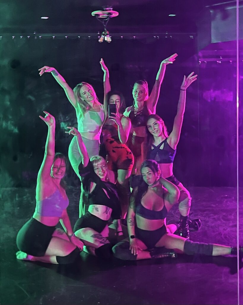 class photo of women in a beginner floorwerk class posing in green and purple lighting