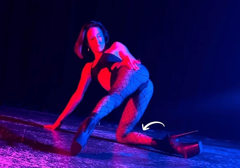 dancer in dramatic red and blue studio lighting with leg extended showing off black fishnet stockings